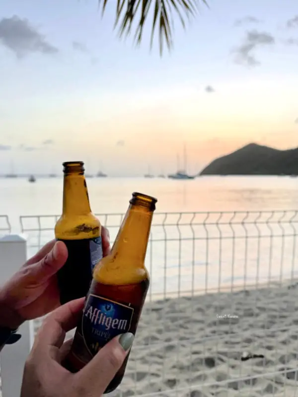 deux personnes trinquent avec des bouteilles de bière sur fond decoucher de soleil à Grande anse martinique